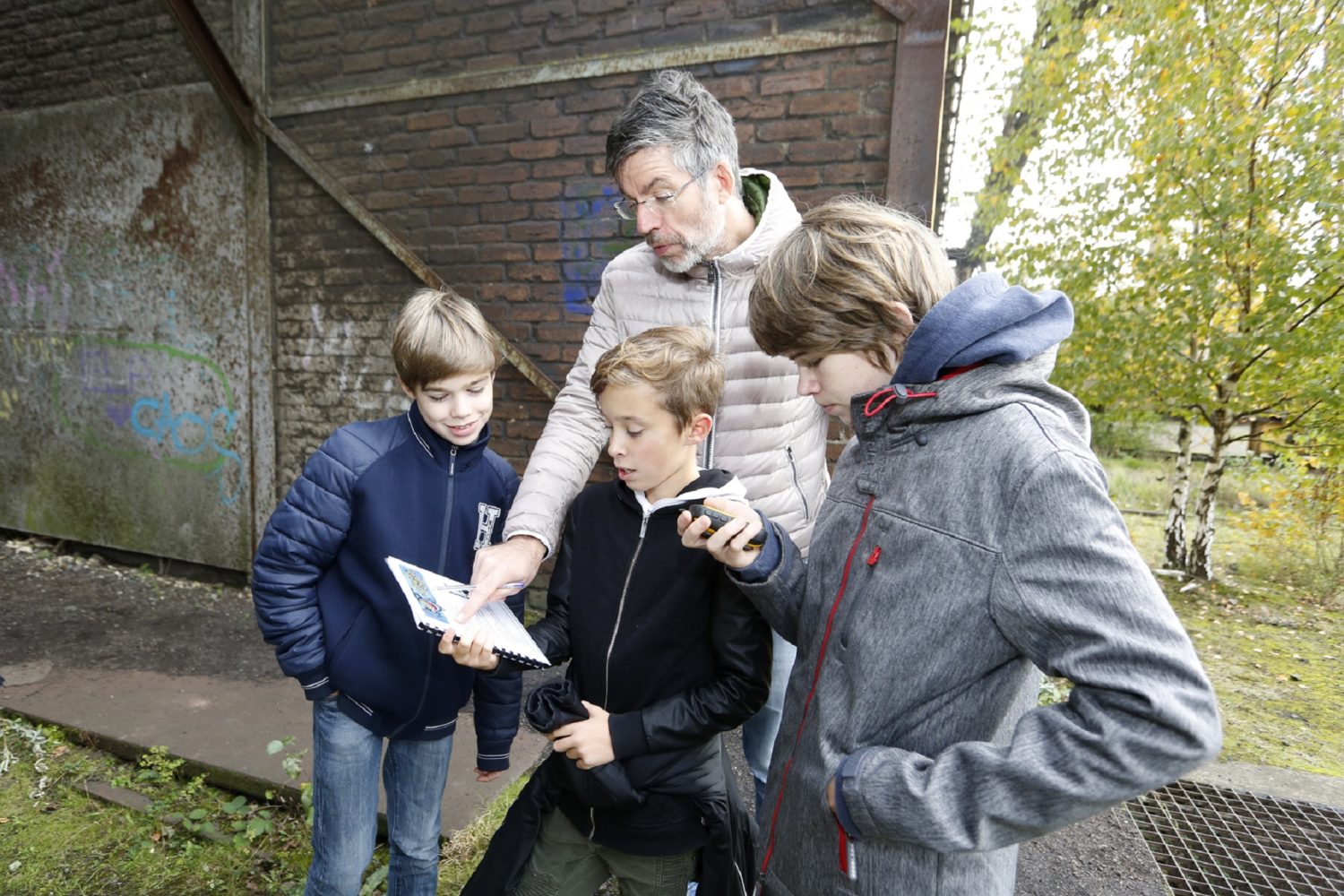 Vater und drei Kinder spielen machen das geocaching im Landschaftspark Duisburg-Nord